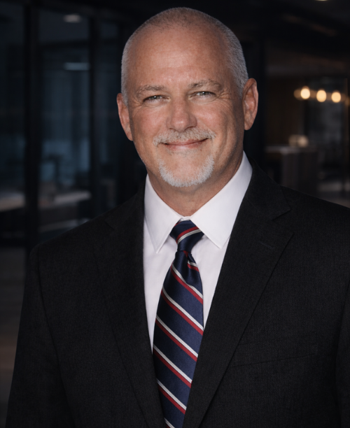 Mark Edward Compo, public adjuster at Rockwall National Public Adjusters, smiling in a professional suit and tie, with a blurred office background.